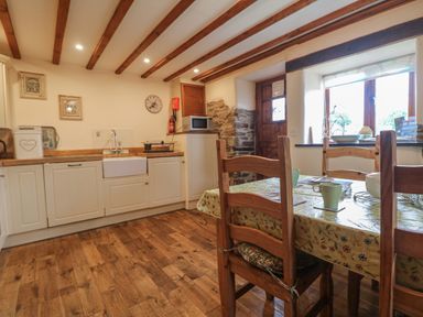 A kitchen with wooden floor cabinets a dining table with chairs and a window at Post House in Holsworthy