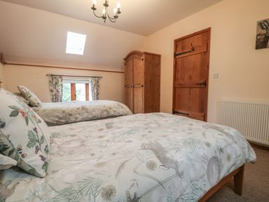 A bedroom with two beds with patterned bedding a wooden wardrobe a wooden door a window with curtains and a ceiling light at Post House in Holsworthy