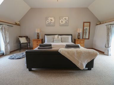 A bedroom with a bed flanked by two wooden nightstands and lamps a chair a mirror and curtains at Post House in Holsworthy