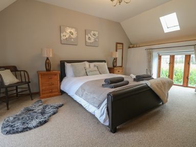 A bedroom with a double bed wooden side tables lamps chair and a window at Post House in Holsworthy