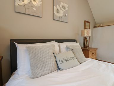 A bedroom with a bed with pillows and a wooden nightstand with a lamp and mirror at Post House in Holsworthy