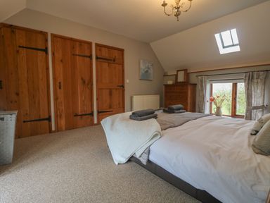 A bedroom with a bed, folded towels, wooden wardrobe doors, a dresser with a mirror, and windows at Post House in Holsworthy