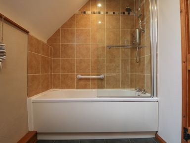 A bathroom with a bathtub and shower fixture with beige tiled walls at Post House in Holsworthy