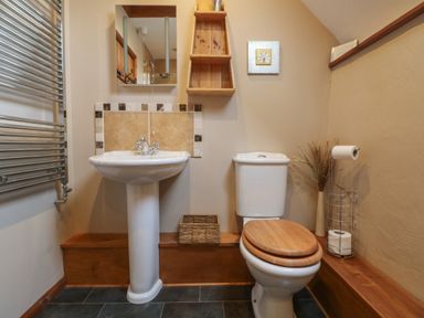 A bathroom with a pedestal sink a toilet with wooden seat a mirror a wall shelf and a towel radiator at Post House in Holsworthy