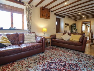 A living room with two brown leather sofas a patterned rug exposed wooden beams and a lamp at The Croft in Holsworthy