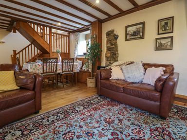A living room with brown leather sofas a floral rug a wooden dining table with chairs and wooden stairs at The Croft in Holsworthy