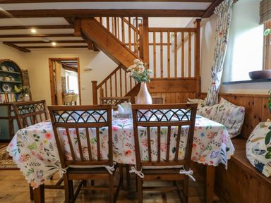 A dining area with wooden chairs and a table with floral tablecloth and vase of flowers near wooden stairs at The Croft in Holsworthy