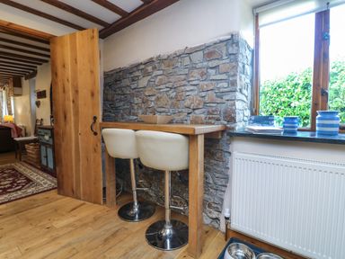 A wooden bar table with two white bar stools by a stone wall and window with blue ceramic jars at The Croft in Holsworthy