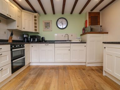 A kitchen with white cabinets wooden floor black countertop and appliances including oven coffee maker and microwave at The Croft in Holsworthy