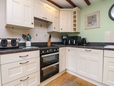 A kitchen with white cabinets black appliances and wooden floor at The Croft in Holsworthy