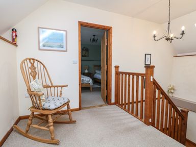 A landing area with a wooden rocking chair next to a doorway and wooden stair railing at The Croft in Holsworthy
