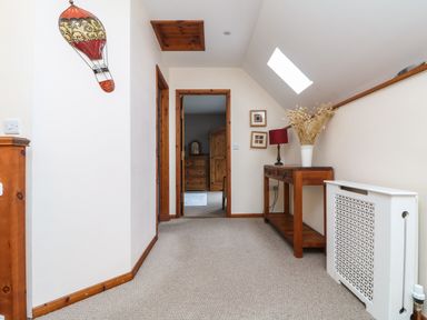 A hallway with a wooden side table holding a lamp and dried flowers a wall-mounted hot air balloon decoration and a view into a bedroom at The Croft in Holsworthy
