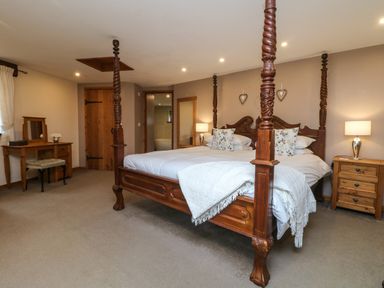 A bedroom with a carved wooden four-poster bed bedside tables a wooden dressing table and a wooden door at The Croft in Holsworthy