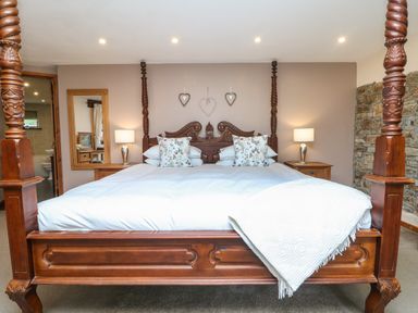 A bedroom with a wooden four-poster bed bedside tables lamps a mirror and an open door showing a bathroom at The Croft in Holsworthy