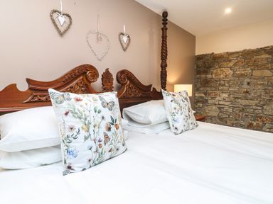 A bedroom with a carved wooden headboard floral pillows and a stone wall at The Croft in Holsworthy