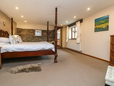 A bedroom with a four-poster bed carpeted floor and a stone accent wall at The Croft in Holsworthy