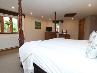 A bedroom with a four poster bed a window with a vase of flowers a dresser with a television and a vanity table at The Croft in Holsworthy