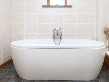 A bathroom with a standalone bathtub and a window above it at The Croft in Holsworthy
