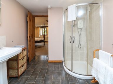 A bathroom with a glass shower enclosure sink with a wicker drawer unit and wooden door leading to a bedroom at The Croft in Holsworthy