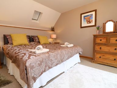 A bedroom with a double bed yellow pillows a wooden dresser and a framed picture of a cow at The Croft in Holsworthy