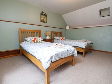 A bedroom with two single wooden beds with floral bedding and a bedside table with a lamp at The Croft in Holsworthy