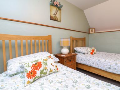 A bedroom with two wooden beds a bedside table with a lamp and floral bedding at The Croft in Holsworthy
