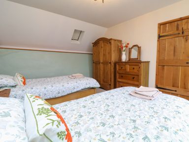 A bedroom with two single beds a wooden wardrobe and chest of drawers with a vase of flowers at The Croft in Holsworthy