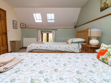 A bedroom with two single beds with floral bedding a wooden nightstand with a lamp a wicker laundry basket and skylights at The Croft in Holsworthy