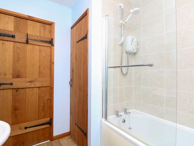 A bathroom with a bathtub shower combination tiled walls wooden doors and a wooden floor at The Croft in Holsworthy