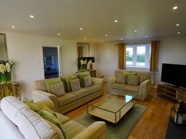 A living room with three sofas a glass coffee table a television and a window at Holly Edge in Moorsholm