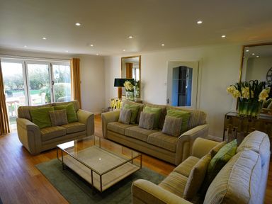A living room with three sofas a glass coffee table wooden floor and a large window with yellow curtains at Holly Edge in Moorsholm