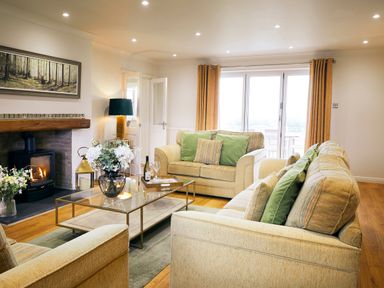 A living room with beige sofas green cushions a glass coffee table with flowers a fireplace and yellow curtains at Holly Edge in Moorsholm