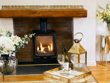 A fireplace with wood burning stove a tray with wine bottle and glasses on a glass table at Holly Edge in Moorsholm