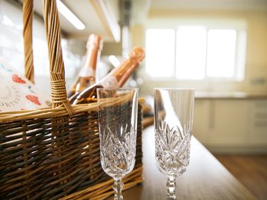 Two crystal champagne glasses in front of a wicker basket with bottles in a kitchen at Holly Edge in Moorsholm