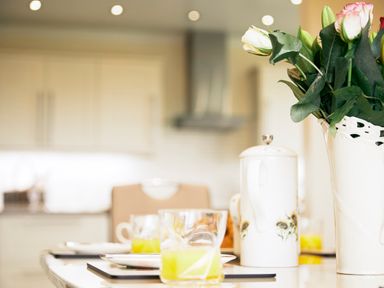 A kitchen table with a vase of flowers a teapot and glasses of orange juice at Holly Edge in Moorsholm