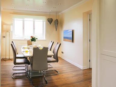 A dining room with a table and six chairs a floor lamp two heart shaped wall decorations and a wall mounted TV at Holly Edge Moorsholm