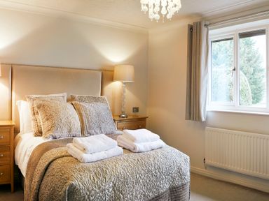 A bedroom with a bed with pillows and folded towels bedside tables with lamps and a window with curtains at Holly Edge in Moorsholm