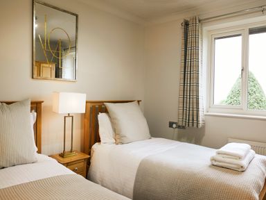A bedroom with two single beds a nightstand lamp a window with plaid curtains and towels on one bed at Holly Edge Moorsholm