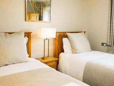 A bedroom with two single beds a nightstand with a lamp a wall mirror and plaid curtains at Holly Edge in Moorsholm
