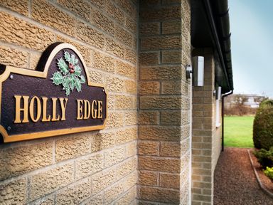 A brick house exterior with a holly edge sign and a green lawn at Holly Edge in Moorsholm