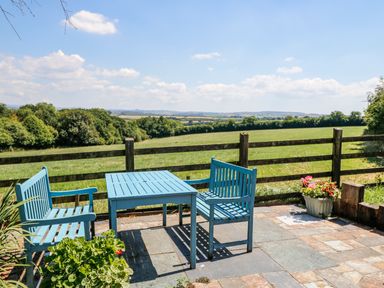 A patio with a blue table and benches overlooking a green field with trees at Janes Place in Lifton