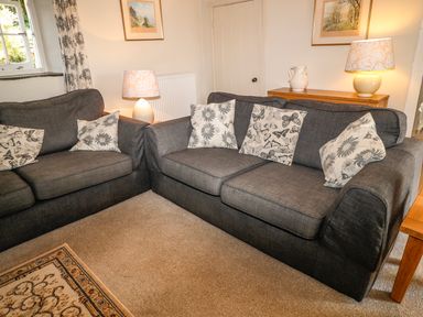 A living room with two dark sofas with patterned cushions two lamps and framed pictures on walls at Janes Place in Lifton