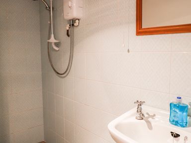 A bathroom with a showerhead and white sink with blue handwash at Janes Place in Lifton