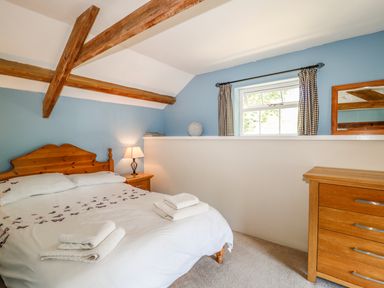 A bedroom with a wooden bed, bedside table with lamp, wooden dresser, window with checkered curtains and wooden beams at Janes Place in Lifton