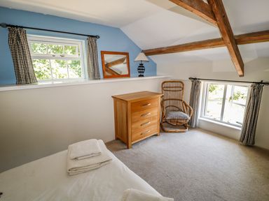 A bedroom with wooden chest of drawers a wicker chair and two windows with checkered curtains at Janes Place in Lifton