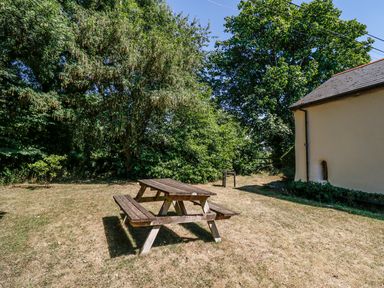 A garden with a wooden picnic table a barbecue and a house wall at Janes Place in Lifton
