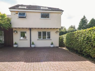 A driveway with potted plants in front of a two-story house bordered by a hedge at Palm Court Burton-in-Kendal
