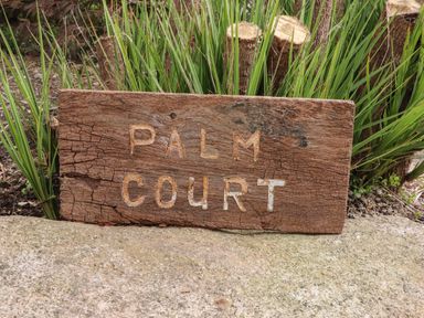 A wooden sign with the text Palm Court in front of green plants at Palm Court in Burton-in-Kendal