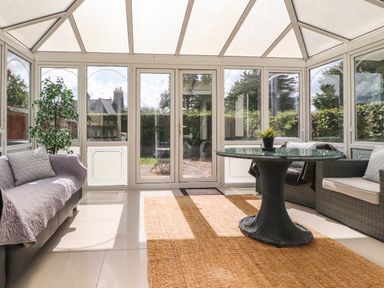 A conservatory with a glass table and wicker chairs and sofas with cushions at Palm Court in Burton-in-Kendal