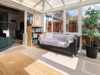 A sunroom with a black sofa covered with a light quilt next to a wooden bookshelf and a potted plant at Palm Court in Burton-in-Kendal